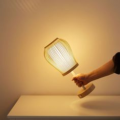 a hand holding a light that is on top of a white table with a wooden base