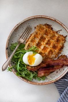 a plate with bacon, waffles and eggs on it next to a fork