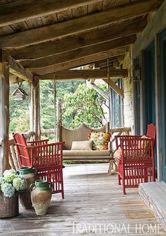 a porch with red chairs and potted plants on the front porch, covered in wood planks