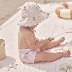 a baby sitting on the beach playing with sand and wearing a sunhat while holding a toy