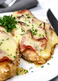 two pieces of meat covered in cheese and parsley on a plate with a knife and fork