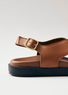 a woman's tan sandal with black soles and a gold buckle on the side