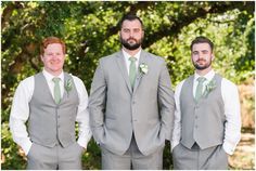 three men in grey suits and green ties posing for the camera with trees in the background