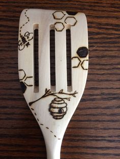 a wooden spoon with bees and honeycombs painted on the side, sitting on a table