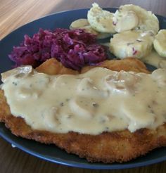 a blue plate topped with fried chicken covered in gravy and veggies