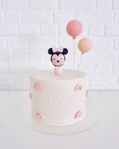 a white cake topped with a minnie mouse topper and two balloons on top of it