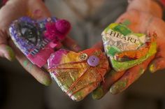 two hands are holding small pieces of art made out of colored paper and buttons with the words heart on them