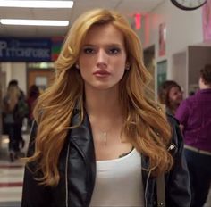 a woman with long red hair is standing in an airport hallway and looking at the camera