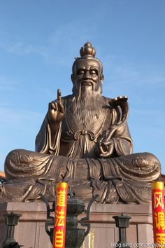 a statue of a man sitting in front of a building with chinese writing on it