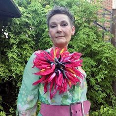 an older woman wearing a pink and green dress with a large flower on it's neck