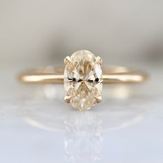 an oval cut yellow diamond sits on top of a white surface, in front of the camera