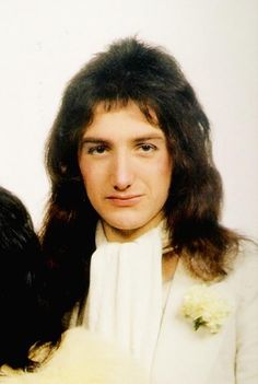 a woman with long hair wearing a white suit and flower in her lap, looking at the camera