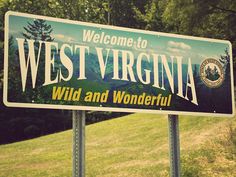 a welcome sign to west virginia in front of some trees and grass on the side of a hill