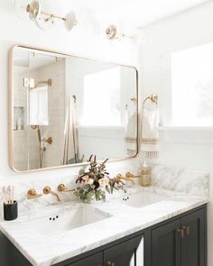 a bathroom with marble counter tops and gold accents on the mirror above the double sink