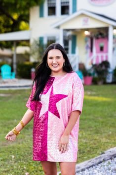 a woman standing in front of a house wearing a pink dress and gold bracelets