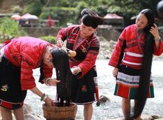 three women in traditional dress are washing the water from a wooden bucket while another woman looks on