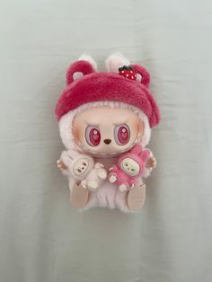 a small stuffed animal wearing a red hat and holding a teddy bear in its arms