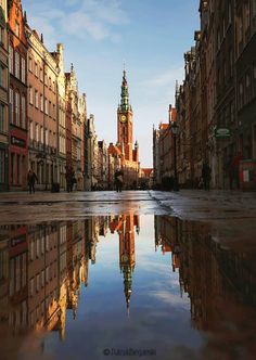 a city street with buildings reflecting in the water and a clock tower at the top