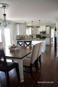 a dining room table and chairs in front of an open kitchen with white cabinets, wood floors