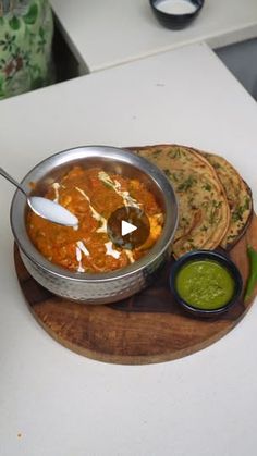 there is a bowl of soup and some bread on the table with green sauces