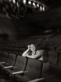 a black and white photo of a woman sitting in an empty theater seat with her hand on her head