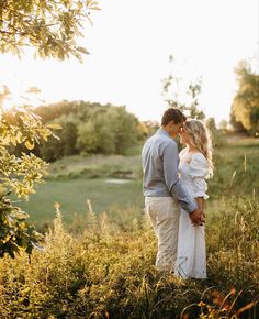 a man and woman standing next to each other in tall grass with the sun behind them