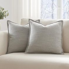 two pillows sitting on top of a couch next to a vase with flowers in it