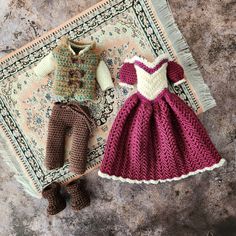 two crocheted dolls are laying next to each other on a rug, one is wearing a dress and the other has a sweater