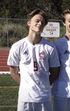 two young men standing next to each other on a soccer field