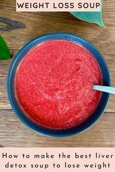 a blue bowl filled with red liquid next to a green leaf on top of a wooden table