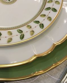 three plates with gold trim and green leaves on the rims, all stacked together