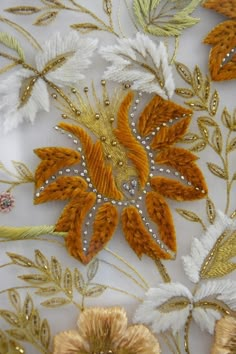 an embroidered fabric with gold, white and orange flowers on it's side is shown