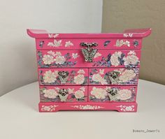 a pink dresser with flowers and butterflies painted on the drawers is sitting on a table