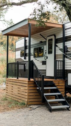 a small white and black trailer parked next to a tree with stairs leading up to it