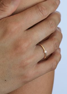 a woman's hand wearing a gold ring with a diamond on the middle finger