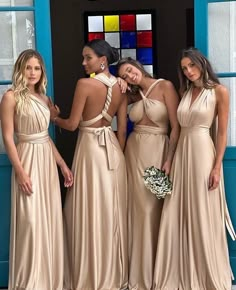 four beautiful women standing in front of a blue door wearing long dresses and holding bouquets