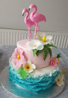 a pink and blue cake with two flamingos on top, sitting on a table