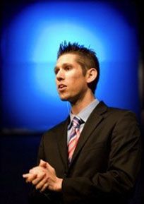 a man wearing a suit and tie standing in front of a blue background with his hands folded