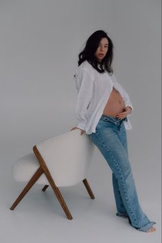 a pregnant woman leaning on a chair with her stomach exposed and looking at the camera