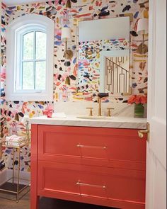 the bathroom is decorated with colorful wallpaper and gold fixtures, along with a red vanity