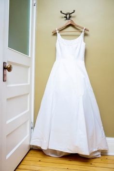 a white dress hanging on a wall next to a door with a hanger in front of it