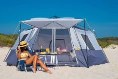 a woman sitting in a chair next to a tent on the beach with a drink