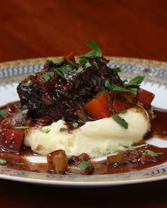 a plate with mashed potatoes, meat and gravy on it sitting on a wooden table