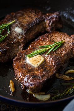 two steaks are being cooked in a skillet with onions and herbs on the side