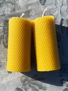 two yellow candles sitting on top of a bed covered in beeswatche paper