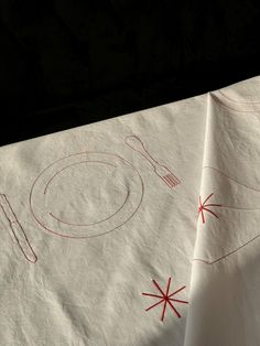 two napkins with red thread on them are sitting on a tablecloth that has utensils and spoons drawn on it