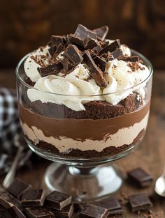 a dessert with chocolate and whipped cream in a glass dish on a table next to spoons