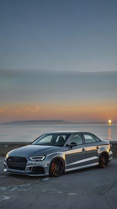 a silver car parked on the side of a road near the ocean at sunset or dawn