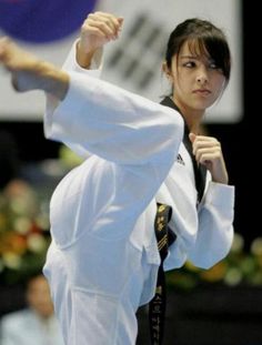 a woman is doing karate in front of an audience at a competition, with her arm raised