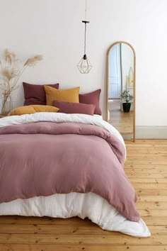 a bed with pink and yellow pillows in a bedroom next to a mirror on the wall